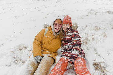 Fröhliche Frauen in warmer Kleidung sitzen im Schnee - VBUF00001