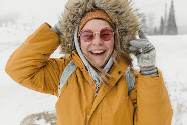 Glückliche Frau mit Sonnenbrille und Pelzjacke genießt im Schnee - VBUF00002