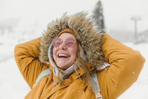 Glückliche Frau in Pelzjacke genießt den Schneefall im Urlaub - VBUF00003