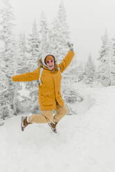 Cheerful woman jumping over snow in forest - VBUF00004