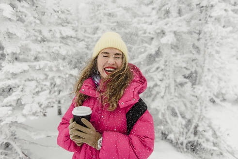 Fröhliche Frau mit Einweg-Kaffeetasse genießt den Schneefall - VBUF00005