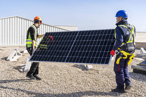 Techniker tragen Solarmodul an einem sonnigen Tag - DLTSF02734