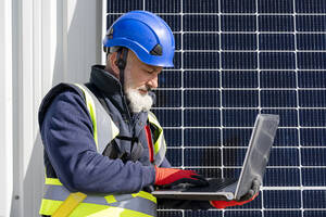 Ingenieur mit Helm bei der Arbeit am Laptop im Solarkraftwerk - DLTSF02746