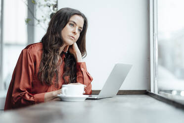 Contemplative woman with laptop in cafe - KNSF09355