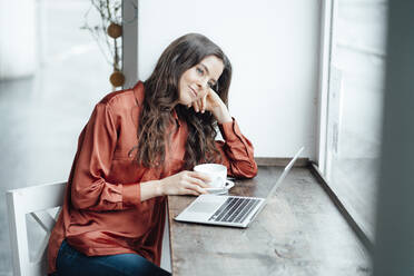 Smiling woman with coffee cup day dreaming in cafe - KNSF09356