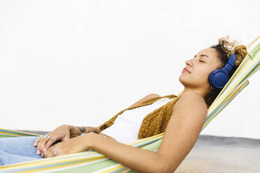 Woman listening music through headphones lying on hammock - MRAF00848