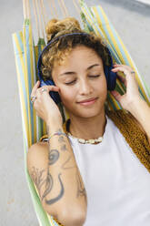 Beautiful woman with eyes closed listening music through headphones on hammock - MRAF00852
