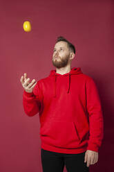 Mann spielt mit Zitrone vor rotem Hintergrund - IYNF00056
