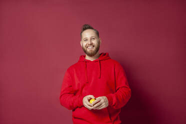 Smiling man with lemon against red background - IYNF00057