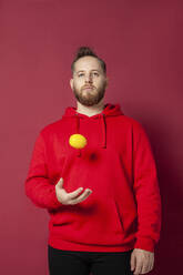 Man playing with citrus fruit against red background - IYNF00059