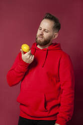Young man looking at lemon in studio - IYNF00061