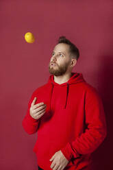 Mann spielt mit Zitrone vor rotem Hintergrund - IYNF00068