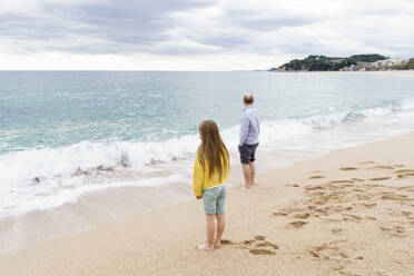 Vater und Tochter stehen an der Küste am Strand - KMKF01784