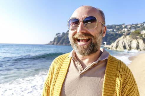 Mann mit Sonnenbrille lachend am Strand am Wochenende - KMKF01795