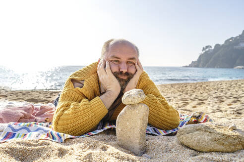 Man with hands on chin looking at stones on beach - KMKF01799