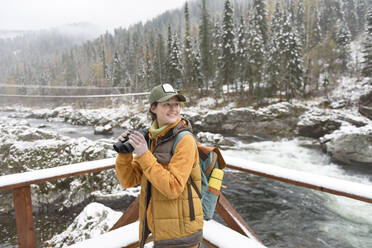 Glückliche Frau mit Fernglas genießt Wochenende am Fluss im Winter - VBUF00020