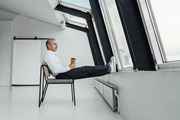 Businessman with disposable coffee cup sitting on chair at office - VPIF05450