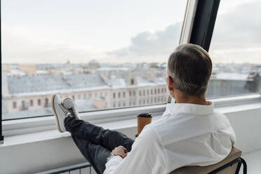 Businessman with disposable coffee cup looking through window in office - VPIF05453