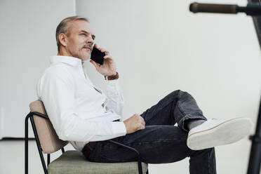 Businessman talking on mobile phone sitting on chair at work place - VPIF05456