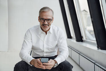 Lächelnder Geschäftsmann mit Smartphone im Büro - VPIF05463