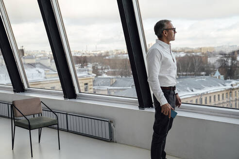 Geschäftsmann schaut durch ein Fenster im Büro stehend - VPIF05465