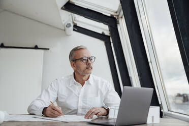 Thoughtful businessman with laptop on desk in office - VPIF05472