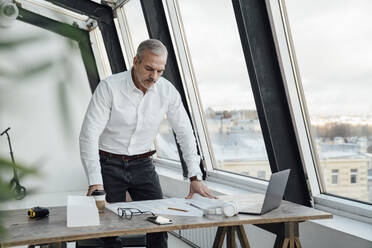 Architect examining paper document on desk at work place - VPIF05483