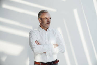 Confident businessman with arms crossed in front of wall - VPIF05491