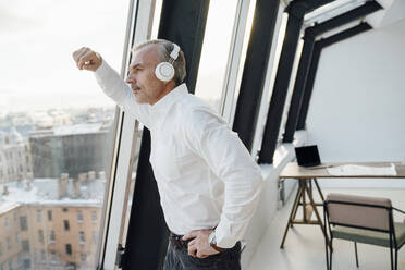 Businessman listening music with headphones looking out of window at work place - VPIF05494