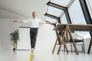 Businessman walking over yellow striped marking on floor in office - VPIF05506