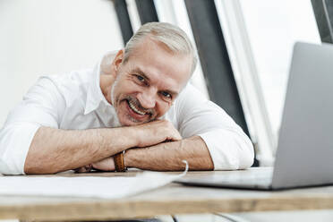 Smiling businessman with laptop on desk in office - VPIF05516