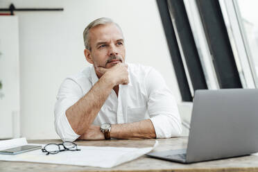 Businessman with hand on chin day dreaming in office - VPIF05518