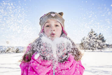 Girl (10-11) in pink jacket blowing snow - TETF00036