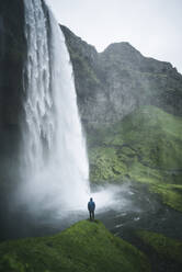 Man standing by Seljalandsfoss waterfall in Iceland - TETF00054