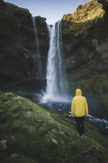 Man wearing yellow raincoat by Kvernufoss waterfall in Iceland - TETF00056