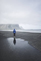 Mann mit blauem Mantel am schwarzen Sandstrand in Kirkjubµjarklaustur, Island - TETF00059