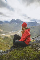 Junge Frau in roter Jacke auf einem Berg sitzend - TETF00075