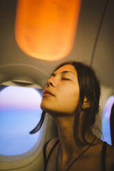 Porträt einer jungen Frau im Flugzeug, beleuchtet mit Sonnenuntergangslicht - TETF00082