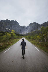 Norwegen, Lofoten-Inseln, Mann geht Straße in Berglandschaft entlang - TETF00085