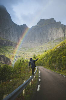 Norwegen, Lofoten-Inseln, Mann balanciert auf Leitplanke mit Bergen und Regenbogen im Hintergrund - TETF00087
