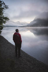 Austria, Plansee, Young man standing by Plansee lake at sunrise - TETF00094