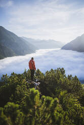 Austria, Plansee, Man standing in trees above valley in clouds in Austrian Alps - TETF00095