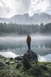 Italien, Carezza, Junger Mann steht auf einem Felsen am Lago di Carezza in den Dolomiten in der Morgendämmerung - TETF00096