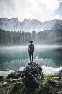 Italien, Carezza, Junger Mann steht auf einem Felsen am Lago di Carezza in den Dolomiten in der Morgendämmerung - TETF00097