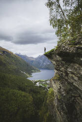 Norwegen, Geiranger, Mann steht am Rand einer steilen Klippe über dem Geirangerfjord - TETF00104