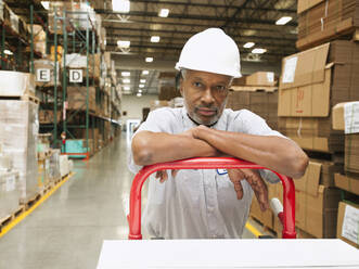 Portrait of man pushing hand truck in warehouse - TETF00135