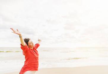 Side view of woman standing with arms up on beach - TETF00190