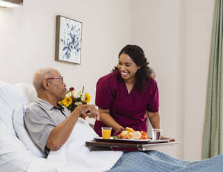 Lächelnde Krankenschwester hängt Essen an einen älteren Mann im Bett - TETF00313
