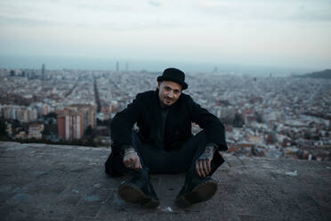 Man wearing black jacket sitting on terrace in front of city - GMLF01264