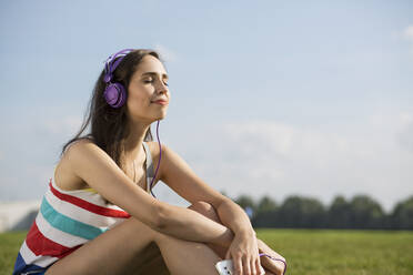 Junge Frau mit Kopfhörern beim Musikhören an einem sonnigen Tag - MIKF00083